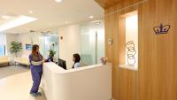 Receptionist and woman in scrubs talk at reception desk.